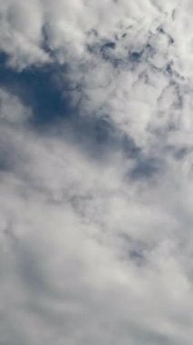 Mavi gökyüzünü kaplayan Stratus bulutları. Atmosferde toplanan bulutların alçak açılı görüntüsü. Zaman ayarlı. Dikey video