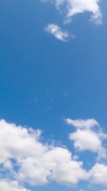 Rüzgar esiyor ve beyaz bulutlar çabucak şekil değiştiriyor. Güneş bulutları aydınlatıyor. Düşük açı. Zaman ayarlı. Dikey video