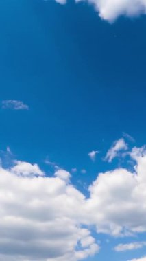 Beyaz kabarık bulutları olan inanılmaz masmavi gökyüzü. Güneş parlıyor ve bulutları aydınlatıyor. Düşük açılı zaman dilimi. Dikey video