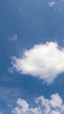 Gökyüzünde süzülen küçük yumuşak bulutlar. Mavi gökyüzü boşalıyor. Düşük açı. Zaman ayarlı. Dikey video