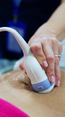 Doğum uzmanı ultrason cihazını hastanın hamile karnında tutuyor. Kadın kliniğe yatırıldı. Kapatın. Dikey video