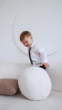 Kanepede ayakta duran mutlu, aktif erkek bebek yastıkları tekmeliyor. Küçük çocuk neşeyle oynuyor. Dikey video.