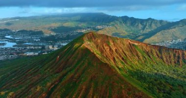 Nadir yeşilliklerle kaplı volkanik kayanın tepesine yaklaşıyoruz. İnsansız hava aracı görüntüleri yoğun yerleşim alanının panoramasını gösteriyor. Oahu Adası, Hawaii, ABD. Hava perspektifi.