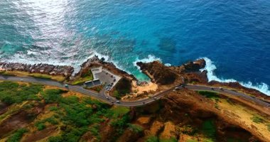 Araç Pasifik Okyanusu 'nun kayalık kıyısındaki otoyoldan geçiyor. Oahu Adası kıyısı, Hawaii, ABD. Hava perspektifi.