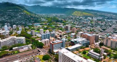 Dağlarla çevrili Honolulu şehir manzarası. Şehrin yukarısında gri, ağır, dramatik bulutlar toplanıyor. Üst perspektif.