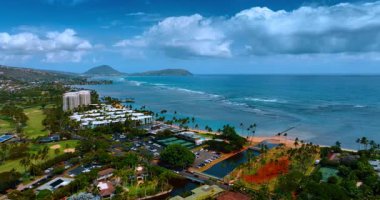 Honolulu, Hawaii 'deki Pasifik Okyanusu kıyılarına yaklaşıyoruz. Suyun üzerinde sallanan palmiye ağaçları ve beyaz bulutlarla kumlu kumsal manzarası. Hava görünümü.
