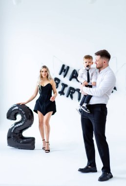 Erkek için ikinci doğum günü partisi. Siyahlı bir kadın, resmi giyinmiş küçük bir çocukla ikinci doğum gününü balonlarla ve dekorasyonlarla kutluyor..