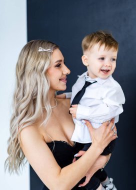 Gülümseyen kadın resmi giyinmiş çocuğu tutuyor. Özel bir durum için giyinmiş bir kadın ve genç bir çocuk arasında neşeli bir an..