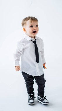 Kravatlı, şık giyinmiş oyuncu çocuk. Beyaz gömlekli ve kravatlı neşeli genç bir çocuk gülümsüyor. Elinde bir oyuncak tutuyor, heyecanını gösteriyor..