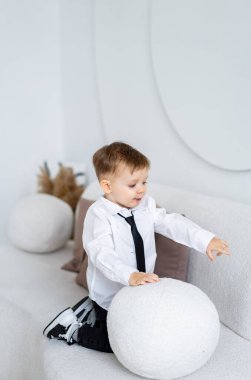Çocuk içeride top oynuyor. Beyaz gömlekli ve kravatlı bir çocuk şık, minimalist bir odada yumuşak bir topla oynamaktan hoşlanır..