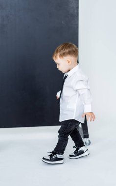 Çocuk modeller şık kıyafetler. Beyaz gömlekli ve siyah kravatlı genç bir çocuk minimalist bir stüdyoda yürür ve kıyafetlerini gösterir..