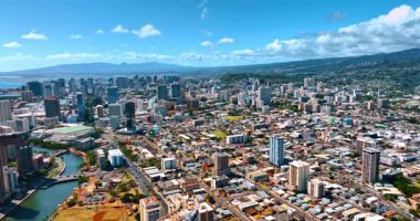 Dağların yamaçlarına uzanan güneşli geniş şehir manzarası. Şehrin panoramasında kabarık bulutlar var. Hava görüntüsü. Honolulu, Hawaii, ABD.