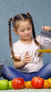 Taze meyve suyu içen kız. Küçük kız bardağa portakal suyu döküyor. Dikey video