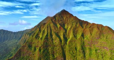 Keskin bir tepe ile yeşil bir dağın çarpıcı manzarası. Lichens kayanın yamaçlarını kaplıyor. Arka planda mavi bulutlu gökyüzü. Hava görünümü.