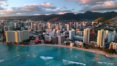 Güzel köpüklü beyaz dalgalar Pasifik Okyanusu kıyılarına yuvarlanıyor. Muhteşem tatil beldesi Waikiki, Honolulu, ABD gün batımında. Gün batımında üzerinde ağır bulutlar olan karanlık dağlar. Hava perspektifi.