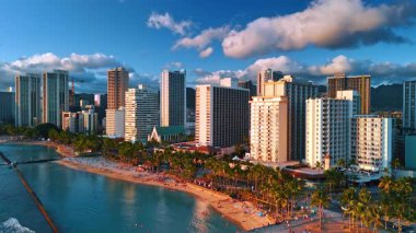 Pasifik Okyanusu kıyısında palmiye ağaçları olan güzel bir sahil. Waikiki Panorama, Honolulu, Hawaii, ABD gün batımında. Arkadaki mavi gökyüzünde kabarık bulutlar. İnsansız hava aracı görüntüleri.