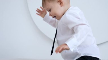 Beyaz tişörtlü, siyah kravatlı sarışın beyaz bebek minderlerle oynuyor. Mutlu çocuk evde eğleniyor..