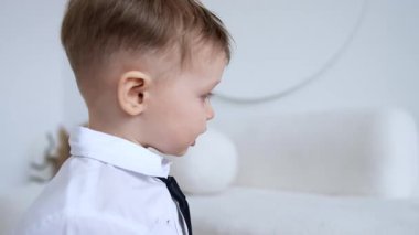 Gömlekli ve kravatlı sevimli bebek evde. Çocuk bir yastık aldı ve kanepeye koydu..