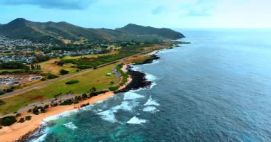 Kıyısında siyah taşlar olan güzel kumlu bir sahil. Dağın eteğinde, arka planda yaşayan bir bölge. Hawaii, ABD.
