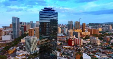 Honolulu, Hawaii, ABD manzarasında aynalı yüzüyle gökdelenlere daha yakın uçuyor. Gün batımında şehrin üzerinde İHA görüntüleri.