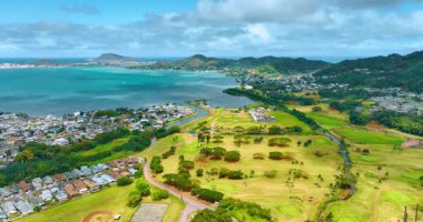 Pasifik Okyanusu 'nun güzel kıyıları. Yeşillikler arasında birden fazla villa var. Golf sahasının üzerinde ağaçların büyüdüğü drone görüntüleri. Arkaplanda yemyeşil dağlar. Hawaii, ABD.