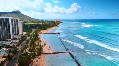 Güzel dalgalar Waikiki, Hawaii, ABD 'deki çarpıcı plajda dalgalanır. Tatilcilerin olduğu otelin üstündeki drone görüntüleri. Arkaplanda Diamond Head Krateri.