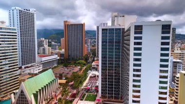 Yüksek binalar arasında yer alan bir otoparka yaklaşıyoruz. Honolulu, Hawaii, ABD 'deki İHA görüntüleri. Arkaplanda dramatik bulutlu manzara.