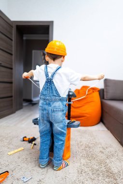 İnşaatçı gibi davranan küçük bir çocuk. Sarı şapkalı bir çocuk oyuncak matkapla oynuyor, rahat bir oturma odasında yaratıcı yapılardan zevk alıyor..