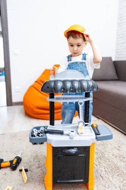 Küçük çocuk oyuncak setiyle oynuyor. Tulumlu ve güvenlik şapkalı bir çocuk, kapalı bir alanda renkli bir oyuncakla meşgul oluyor..