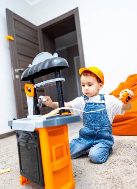 Oyuncak tezgahındaki çocuk. Genç bir çocuk yerde oturuyor, oyuncak tezgahı ve parlak bir odada aletlerle aktif olarak meşgul..