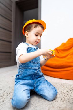 Çocuk parlak odada oyuncakla oynuyor. Parlak turuncu şapkalı bir çocuk, halı kaplı bir odada oyuncakla oynar..