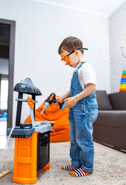 Çocuk içeride oyuncak tezgahıyla oynuyor. Turuncu gözlük takan genç bir çocuk, içeride oyun oynamaya odaklanmış renkli bir oyuncak tezgahıyla meşgul oluyor..