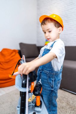 Oyuncak aletlerle oynayan genç inşaatçı. Güvenli kasklı bir çocuk, içeride yaratıcılığını ve hayal gücünü gösteren oyuncak bir inşaat setiyle oynar..