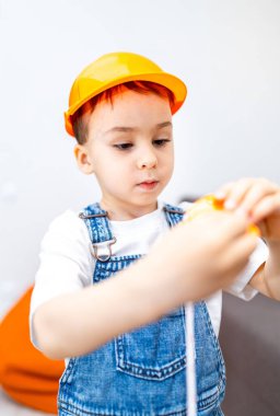 Genç çocuk içeride oyuncak aletlerle oynuyor. İnşaat şapkası takan bir çocuk, parlak bir odada yaratıcı oyunlar sergileyen oyuncak bir aletle dikkatle temas eder..