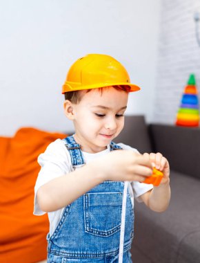 Çocuk oyuncaklarla oynuyor. Sert şapka takan bir çocuk renkli blokları olan bir bina inşa etmekten zevk alır. Parlak, neşeli bir kapalı alanda..