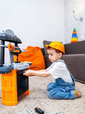 Çocuk aletlerle yaratıcı bir şekilde oynuyor. Turuncu şapkalı bir çocuk oyuncak tezgahı ve ev ortamında aletlerle yaratıcı bir şekilde oynar..