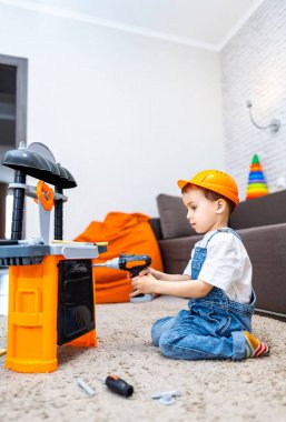 Çocuk oyuncak aletlerle oynuyor. Güvenlik kaskı takmış küçük bir çocuk oyuncak tezgahını tamir ediyormuş gibi yapıyor..