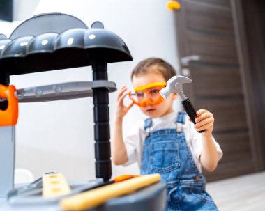 Çocuk aletlerle oynuyor. Güvenlik gözlüğü takan bir çocuk oyuncak bir çekiç tutuyor. Parlak bir odada oyun aleti ile inşa etmeye odaklanmış..