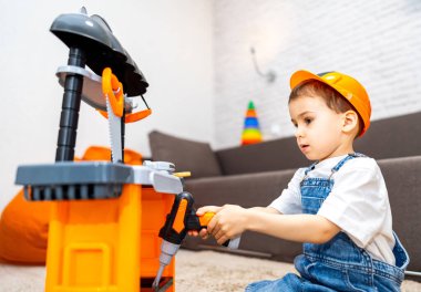 Çocuk oyuncak projesi yapıyor. Küçük bir çocuk oyuncak tezgahıyla meşgul olur, parlak bir odada güvenlik kaskı takıyormuş gibi yapar..