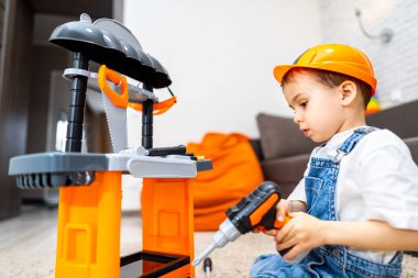 Çocuk oyuncak aletlerle oynuyor. Küçük bir çocuk güvenlik kaskı takarken oyuncak tezgahı kullanıyormuş gibi yapıyor..