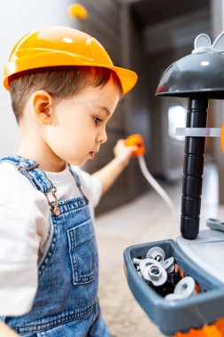 Çocuk oyuncak alet takımıyla oynamaktan hoşlanıyor. Güvenlik şapkası takan küçük çocuk, yumuşak halıda oynarken renkli bir oyuncak setine odaklanıyor..