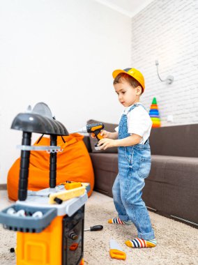 Çocuk oyuncak aletlerle oynuyor. Şapkalı bir çocuk, oturma odasında oyuncak aletler kullanarak etkinlik düzenlemekten zevk alır..