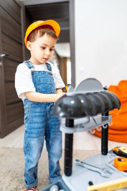 Çocuk içeride oyuncaklarla oynuyor. İnşaat şapkası takan küçük bir çocuk, rahat bir oturma odasında oyuncak tezgahıyla meşgul oluyor..