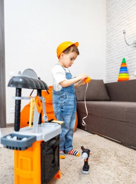 Genç müteahhit yaratıcı bir oyuna dahil oldu. Kot pantolon giyen bir çocuk, parlak bir oturma odasında inşaat oyuncaklarıyla oynar, odak ve yaratıcılık gösterir..