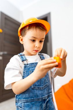 Çocuk içeride bloklarla oynuyor. İnşaat şapkalı bir çocuk oyuncak bloğunu rahat, renkli bir iç mekanda birleştiriyor..