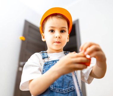 Çocuk içeride yaratıcı bir şekilde oynuyor. Sarı şapkalı bir çocuk parlak bir odada oyuncak bloklarıyla oynar, yaratıcılığını gösterir..