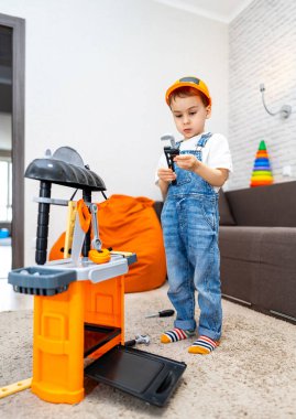 Çocuk içeride oyuncak aletlerle oynuyor. Tulumlu ve kasklı bir çocuk, parlak bir yaşam alanına kurulmuş renkli bir oyuncakla karşılaşır..