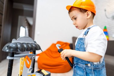 Çocuk numara yapmaktan hoşlanıyor. Sert şapkalı genç bir çocuk, gün boyunca kapalı bir ortamda oyuncak bir aletle oynuyor..