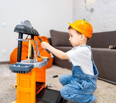 Oyuncak blokları olan bir çocuk. Sert şapkalı bir çocuk, kapalı bir alanda oyuncak bir inşaat setiyle oynuyor, bina faaliyetlerine odaklanmış..