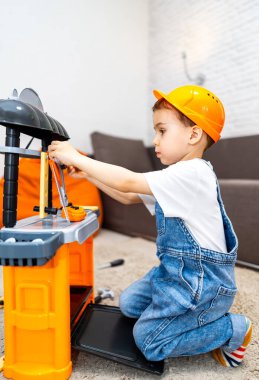 Çocuk oyuncak aletlerle oynuyor. Bir çocuk halıda diz çöküyor, oyun istasyonundaki aletleri toplamaya odaklanmış, konsantrasyon ve neşeyle..